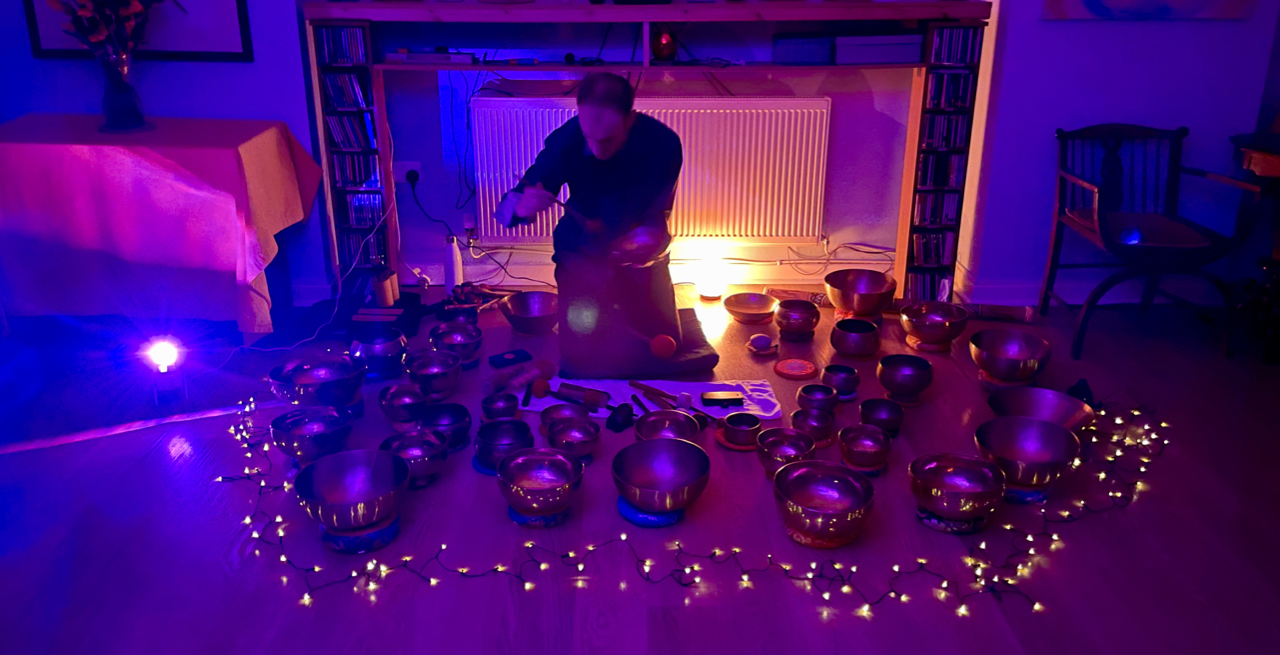 Dr. Nicholas Peters playing a Manipuri Himalayan singing bowl. He is surrounded by over thirty Himalayan singing bowls.